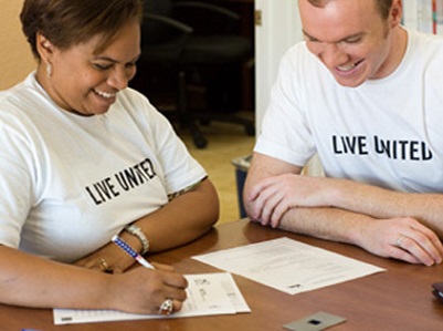 United Way Volunteers photo with a man with brown hair and a white shirt with black Live United Lettering speaking with a woman with short brown hair also wearing a white shirt with black lettering that says live united.