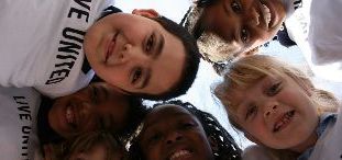 5 children with brown and blonde hair with big smiles wearing white t-shirts with black lettering that says LIVE UNITED in uppercase lettering. The background is white.