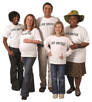 There is a group of people with brown and blonde hair, all are smiling, and one is wearing a hat. A few have brown eyes, the woman and child in front have blue eyes. The woman on the right is wearing a straw hat. All in the photo are wearing a white shirt with uppercase black lettering that says LIVE UNITED.