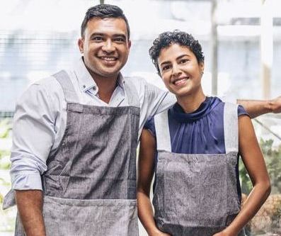 Two individuals, both tan complected with Brown hair and brown eyes. Man has white shirt on and grey coveralls, woman has blue sleeveless shirt with grey coveralls.